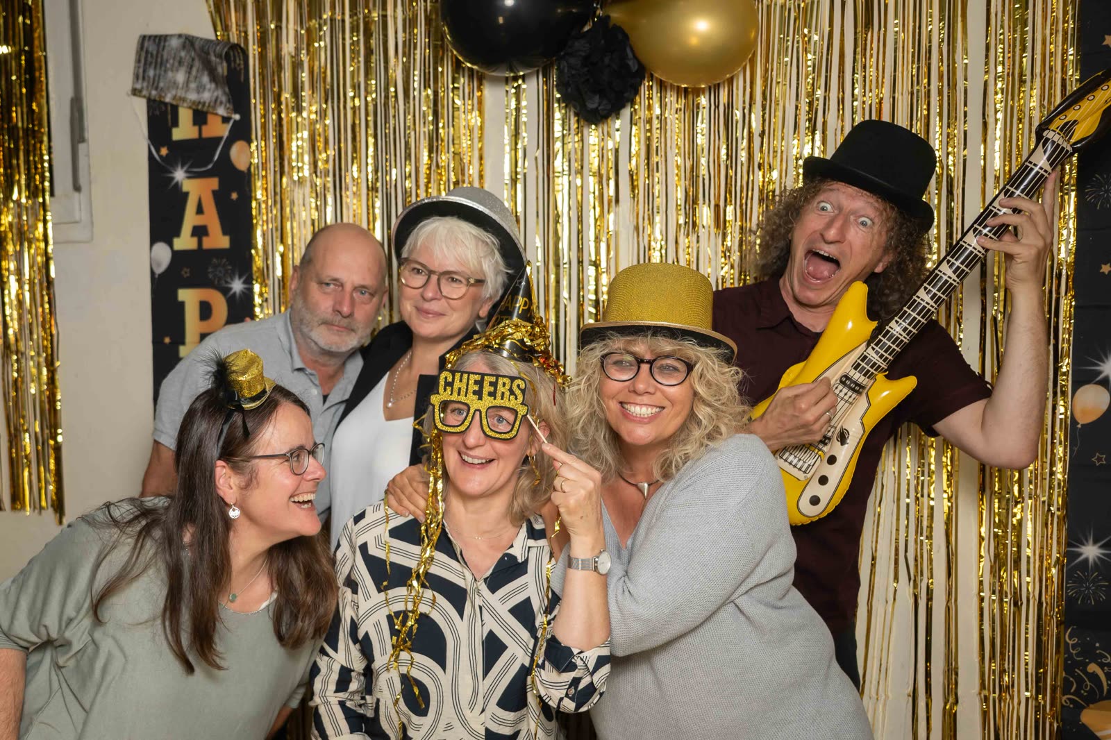 Fröhliche Gruppe mit Partybrillen und Luftgitarre vor goldenem Hintergrund